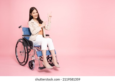 Smiling young Asian businesswoman sitting on wheelchair and pointing to empty copy space isolated on pink background - Powered by Shutterstock