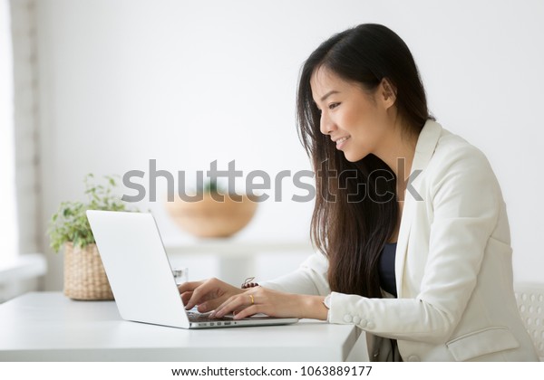 Smiling young asian businesswoman using computer at\
home office workplace, happy korean employee working on laptop,\
attractive japanese or chinese woman student studying communicating\
online with pc