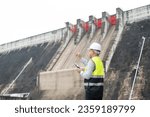 Smiling young Asian civil engineer standing with his arms crossed wearing a helmet and using a walkie-talkie. View and inspect the operation of the dam