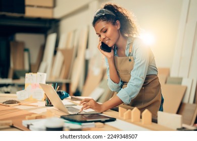 Smiling Young Asian female carpenter using laptop computer while talking to customer on the phone in woodcraft carpentry workshop. - Powered by Shutterstock