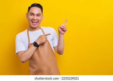 smiling young Asian man 20s barista barman employee wearing brown apron working in coffee shop, pointing finger on advertising area on yellow background. Small business startup concept - Powered by Shutterstock