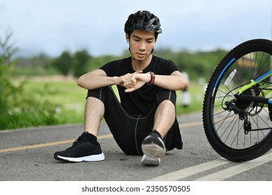 Smiling young Asian man cyclist resting after riding bicycle and checking sport activity progress data on smartwatch - Powered by Shutterstock