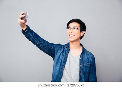 Smiling Young Asian Man Making Selfie Photo On Smartphone Over Gray Background