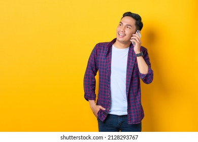 Smiling young Asian man in plaid shirt talking on mobile phone and looking away at copy space isolated on yellow background - Powered by Shutterstock