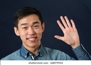 Smiling Young Asian Man Waving His Palm And Looking At Camera