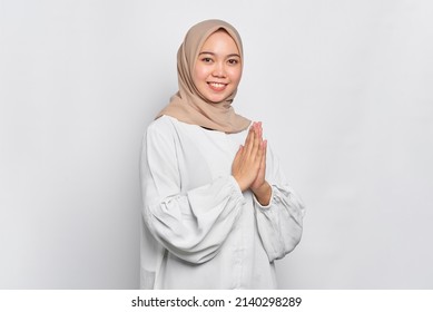 Smiling young Asian Muslim woman gesturing Eid Mubarak greeting isolated over white background - Shutterstock ID 2140298289