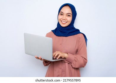 Smiling young Asian muslim woman in pink shirt holding a laptop and looking at camera isolated over white background. People religious lifestyle concept - Powered by Shutterstock