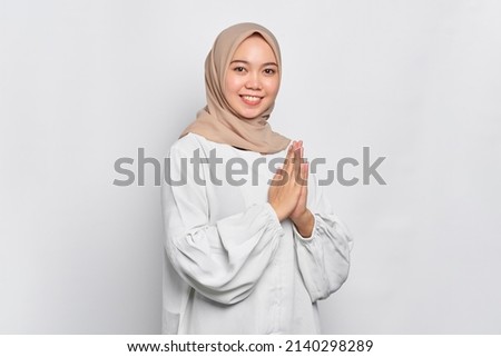 Smiling young Asian Muslim woman gesturing Eid Mubarak greeting isolated over white background