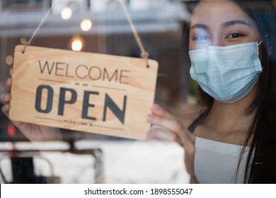 Smiling Young Asian Owner Retail,coffee Shop Woman Turning Sign Board To Open Wearing Face Mask,protect To Pandemic Of Coronavirus, Reopen Store After Close Lockdown Quarantine In Covid To New Normal.