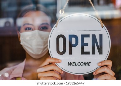 Smiling Young Asian Owner Retail,coffee Shop Woman Turning Sign Board To Open Wearing Face Mask,protect To Pandemic Of Coronavirus, Reopen Store After Close Lockdown Quarantine In Covid To New Normal.