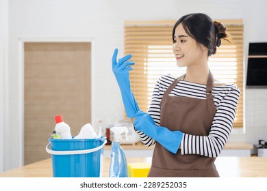 Smiling young asian woman in apron puts on rubber gloves and ready to housework in kitchen room interior. Housewife has fun and many household chores, domestic work and professional cleaning service. - Shutterstock ID 2289252035