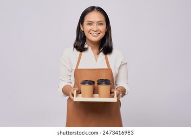 Smiling young Asian woman barista barman employee wearing a brown apron working in coffee shop giving takeaway paper cups of coffee or tea and looking at the camera isolated on white background - Powered by Shutterstock