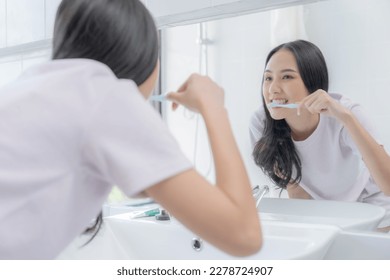 Smiling young Asian woman brushing teeth in bathroom. - Powered by Shutterstock