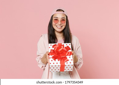 Smiling young asian woman in casual clothes cap glasses isolated on pastel pink wall background. St. Valentine's Day, Women's Day, birthday, holiday concept. Hold red present box with gift ribbon bow