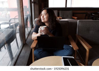 Smiling Young Asian Woman Is Drinking A Cup Of Coffee And Relaxing After Online Working With Black Laptop At Coffee Shop. Lifestyle And Relaxtime Of Businesswoman On Holiday Concept