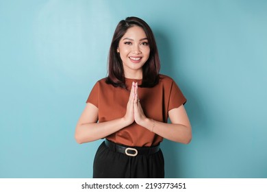 Smiling Young Asian Woman Gesturing Traditional Greeting Isolated Over Blue Background