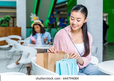 Smiling young asian woman sitting with shopping bags in shopping mall