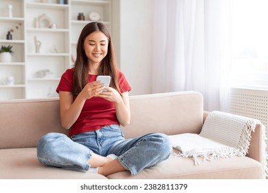 Smiling Young Asian Woman With Smartphone Relaxing On Couch At Home, Happy Millennial Female Using Mobile Phone For Messaging With Friends Or Browsing New App For Shopping While Sitting On Sofa - Powered by Shutterstock