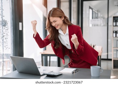 Smiling young asian woman succeeding in business using laptop and computer while doing some paperwork at office. - Shutterstock ID 2321723067