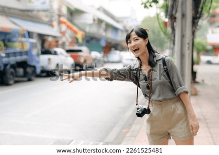 Smiling young Asian woman traveler hitchhiking on a road in the city.