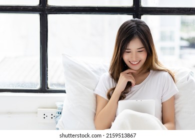 Smiling Young Asian Woman Use Tablet Computer And Scrolling Through Tablet On Bed At Bedroom With Happiness Pretty Girl Always Using Tablet For Social Media Shopping Online Study And Watching Movie