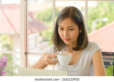 Smiling Young Asian Woman Wear Casual Clothing Working With Computer Laptop And Holding Coffee Mug In Living Room At Home. WFH. Work At Home Concept