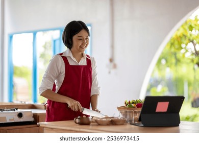 Smiling young asian woman wearing apron, learning to cook from online cooking class, using tablet in kitchen - Powered by Shutterstock