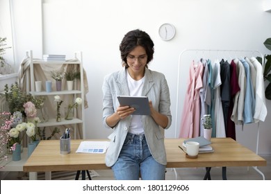 Smiling young attractive professional decorator leaning at table, communicating with clients on computer tablet indoors or using applications for creating sketching new clothing collection in office. - Powered by Shutterstock