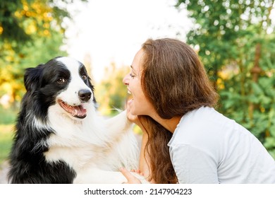 Smiling Young Attractive Woman Playing With Cute Puppy Dog Border Collie On Summer Outdoor Background. Girl Holding Embracing Hugging Dog Friend. Pet Care And Animals Concept