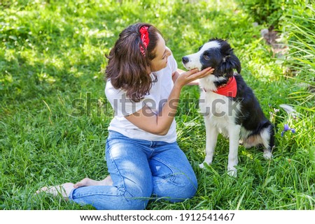Smiling young attractive woman playing with cute puppy dog border collie in summer garden or city park outdoor background. Girl training trick with dog friend. Pet care and animals concept