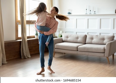 Smiling Young Barefoot Mixed Race Woman Holding On Hands Little Adopted Kid Girl, Twisting Together In Living Room. Happy Mommy Dancing To Music, Having Fun With Excited Small Daughter At Home.