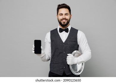 Smiling Young Barista Male Waiter Butler Man 20s Wear White Shirt Vest Elegant Uniform Work At Cafe Hold Mobile Phone With Blank Screen Isolated On Plain Grey Background. Restaurant Employee Concept