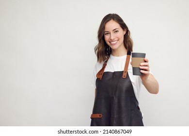 Smiling young barista woman in apron isolated on white background. Looking beautiful and happy with a to-go coffee cup in hand. Concept: serving coffee. - Powered by Shutterstock