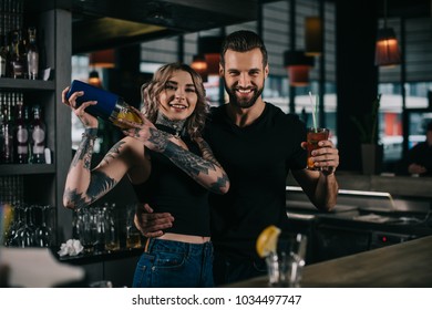 smiling young bartenders preparing alcohol drinks at bar and looking at camera - Powered by Shutterstock