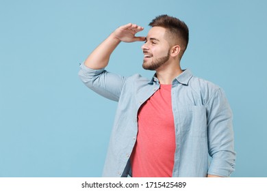 Smiling young bearded guy 20s in casual shirt posing isolated on pastel blue background studio portrait. People lifestyle concept. Mock up copy space. Hold hand at forehead looking far away distance - Shutterstock ID 1715425489