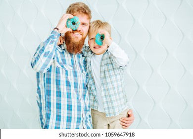 Smiling young bearded hipster man with his cute son having fun while holding donuts on their eyes over white background. - Powered by Shutterstock