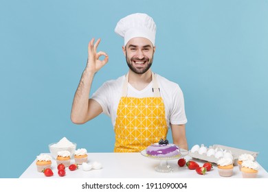 Smiling young bearded male chef or cook baker man in apron white t-shirt toque chefs hat cooking at table isolated on blue background. Cooking food concept. Mock up copy space. Showing OK gesture - Shutterstock ID 1911090004