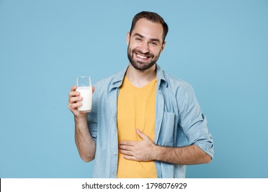 Smiling Young Bearded Man 20s Wearing Casual Clothes Posing Holding In Hand Glass Of Milk Put Hand On Stomach Looking Camera Isolated On Pastel Blue Background Studio Portrait