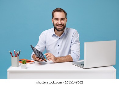 Smiling young bearded man in light shirt sit work at white desk with pc laptop isolated on pastel blue background in studio. Achievement business career concept. Mock up copy space. Hold calculator - Shutterstock ID 1635149662