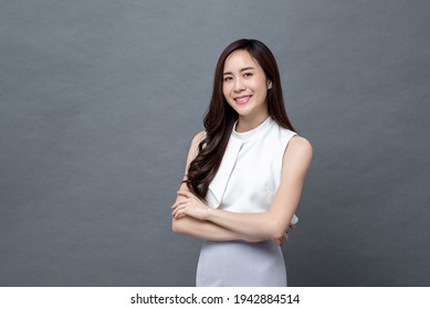 Smiling young beautiful Asian businesswoman looking at camera and doing arm crossed gesture in isolated studio gray background - Powered by Shutterstock