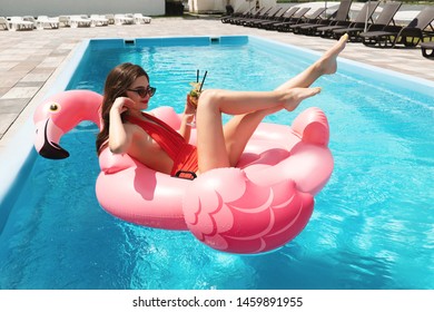 smiling young beautiful brunette woman wearing red sexy swimsuit and sunglasses suntanning in the hotel pool drinking cocktail having great time on vacation