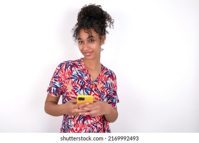 Smiling Young Beautiful Brunette Woman Wearing Colourful Dress Over White Wall Friendly And Happily Holding Mobile Phone Taking Selfie In Mirror.