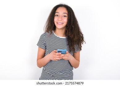 Smiling Young Beautiful Brunette Woman Wearing Striped T-shirt Over White Wall Friendly And Happily Holding Mobile Phone Taking Selfie In Mirror.