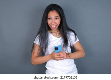 Smiling Young Beautiful Brunette Woman Wearing Grey T-shirt Over White Wall Friendly And Happily Holding Mobile Phone Taking Selfie In Mirror.