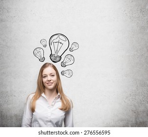 Smiling young beautiful business lady is thinking about new innovative ideas. Light bulbs are drawn on the concrete wall behind the lady. - Shutterstock ID 276556595