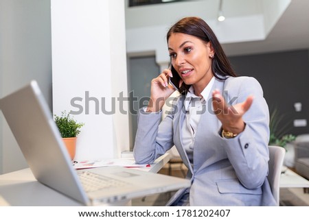 Smiling young beautiful business woman working on laptop in bright modern home office. Business woman talking on her mobile phone while working from home