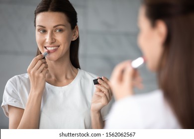 Smiling Young Beautiful Lady Holding Apply Nude Color Lipstick On Lips Get Ready In Morning, Happy Sexy Gorgeous Attractive Woman Look In Mirror Doing Make Up Routine Put Cosmetic On Face In Bathroom