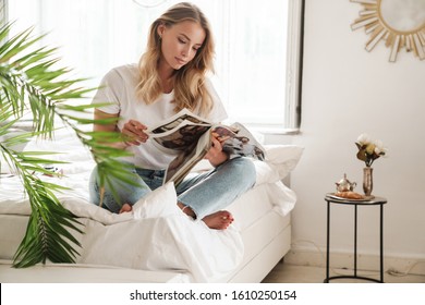 Smiling young beautiful woman reading magazine while sitting on a couch at the living room - Powered by Shutterstock