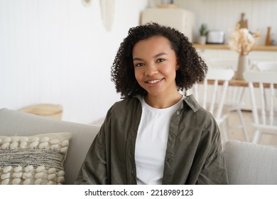 Smiling young biracial girl with afro hairstyle sits on sofa in cozy living room at home. Happy friendly biracial teen lady relaxing sitting on couch, looking at camera on weekend day. - Powered by Shutterstock