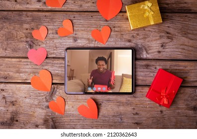 Smiling young biracial man with gifts seen in digital tablet during video call on valentine day. unaltered, online dating, video call, wireless technology, gift and distant valentine day celebration.